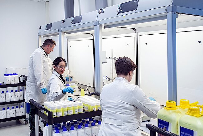 Drei Mitarbeiter führen Ab- und Umfüllarbeiten im Labor durch